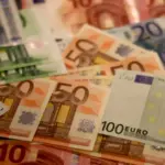 Κέρματα και χαρτονομίσματα σε στοίβα, με φόντο οικονομικά στοιχεία
