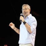 Ο Θοδωρής Αθερίδης μιλά σε εκδήλωση με φόντο σχετικό δημοσιογραφικό πλάνο