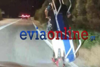 Δύο άτομα μεταφέρουν ξαπλώστρα θαλάσσης πάνω σε ηλεκτρικό πατίνι σε δρόμο από το Αλιβέρι προς τη Χαλκίδα