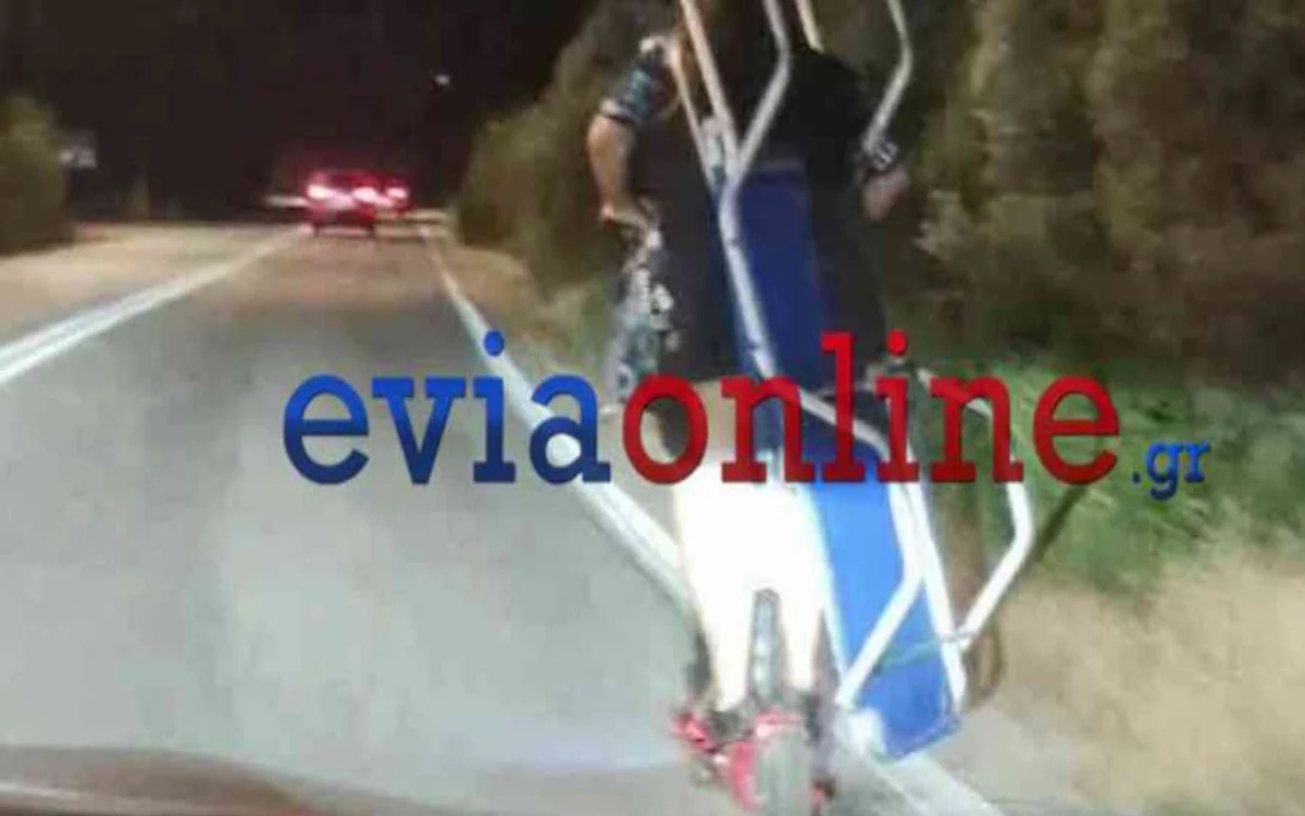 Δύο άτομα μεταφέρουν ξαπλώστρα θαλάσσης πάνω σε ηλεκτρικό πατίνι σε δρόμο από το Αλιβέρι προς τη Χαλκίδα